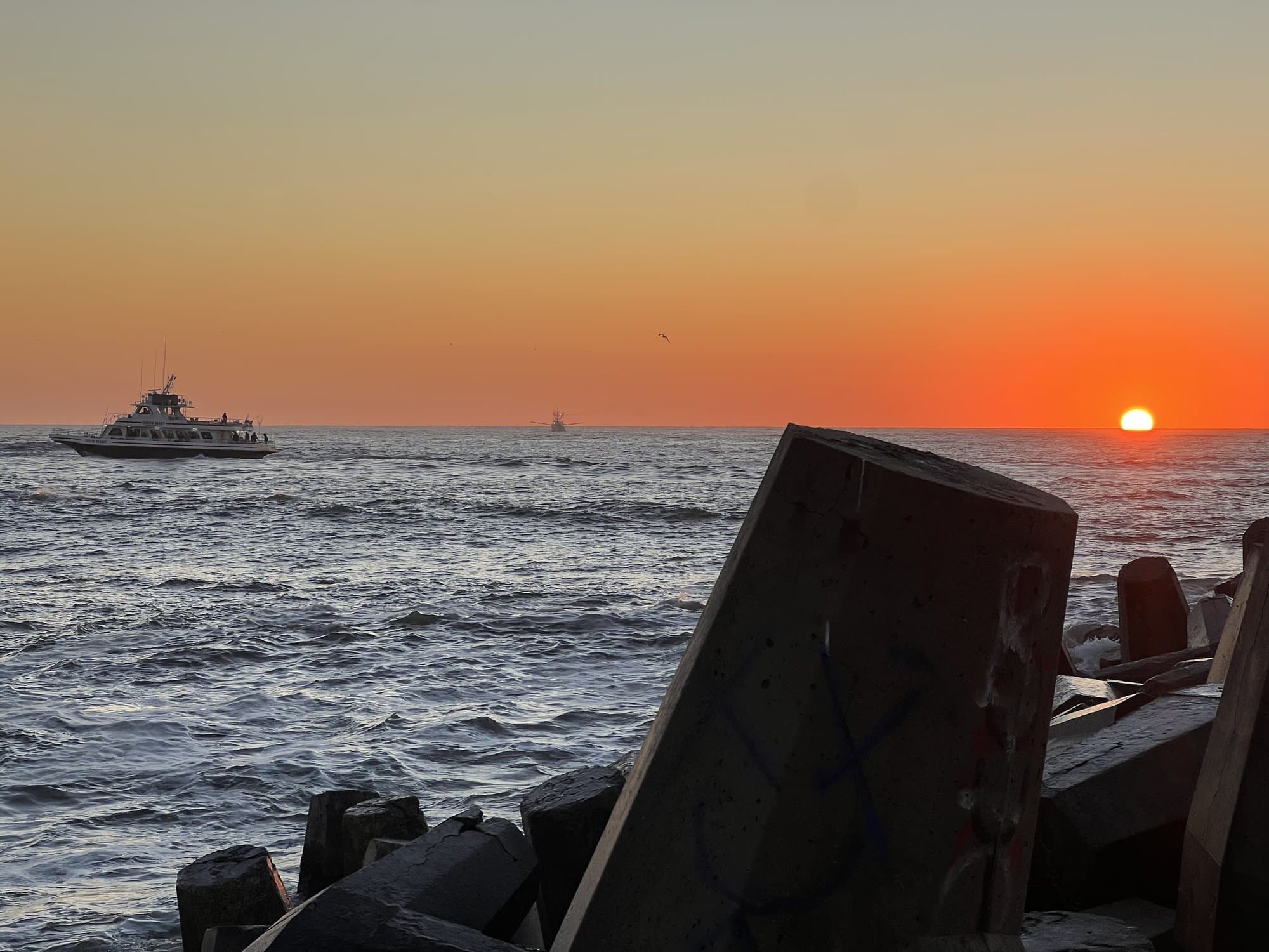 Concrete jetty blocks at sunset with a party boat offshore