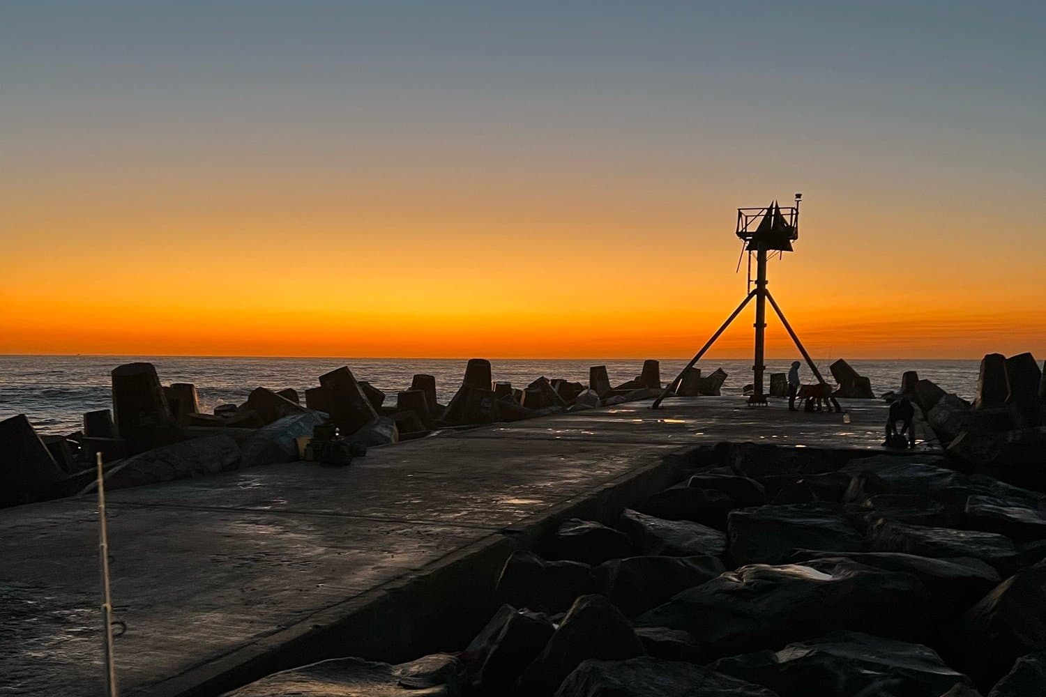 Jetty walkway at sunrise with a light tower and a fishing rod